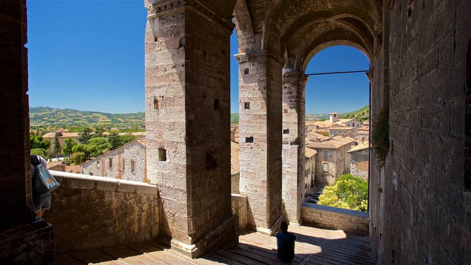 An ancient stone archway overlooking a historic town with terracotta rooftops.