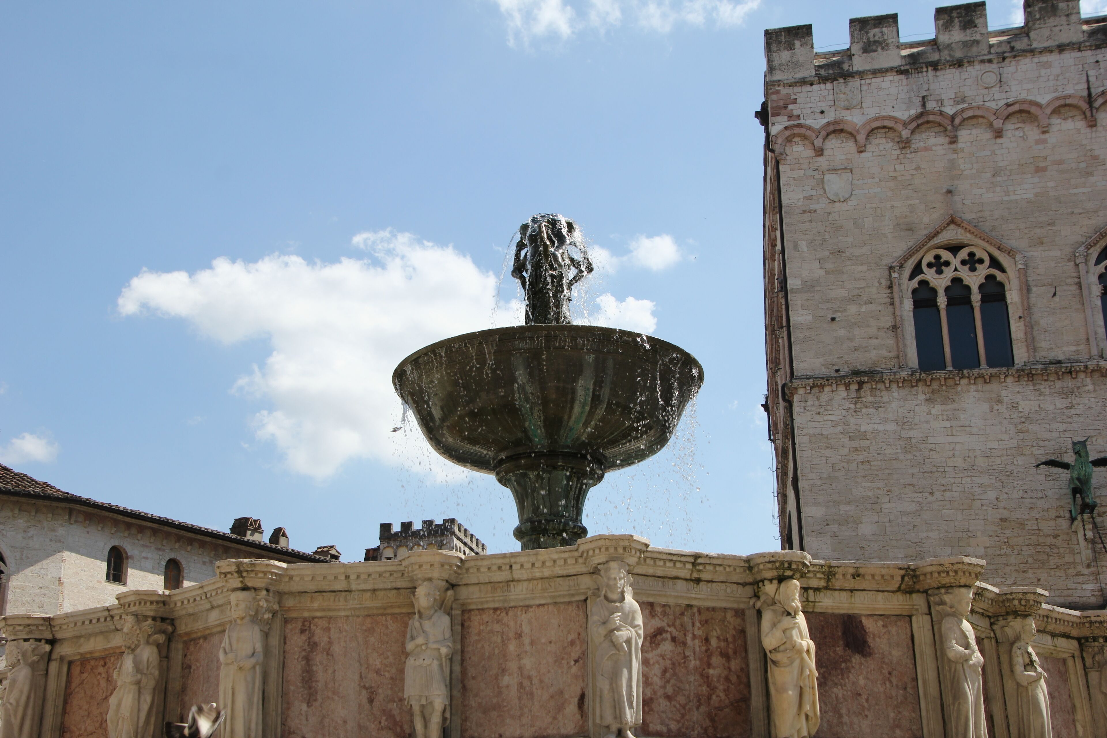 Una fuente histórica con una estatua, rodeada de columnas ornamentales, frente a un edificio que parece un castillo.