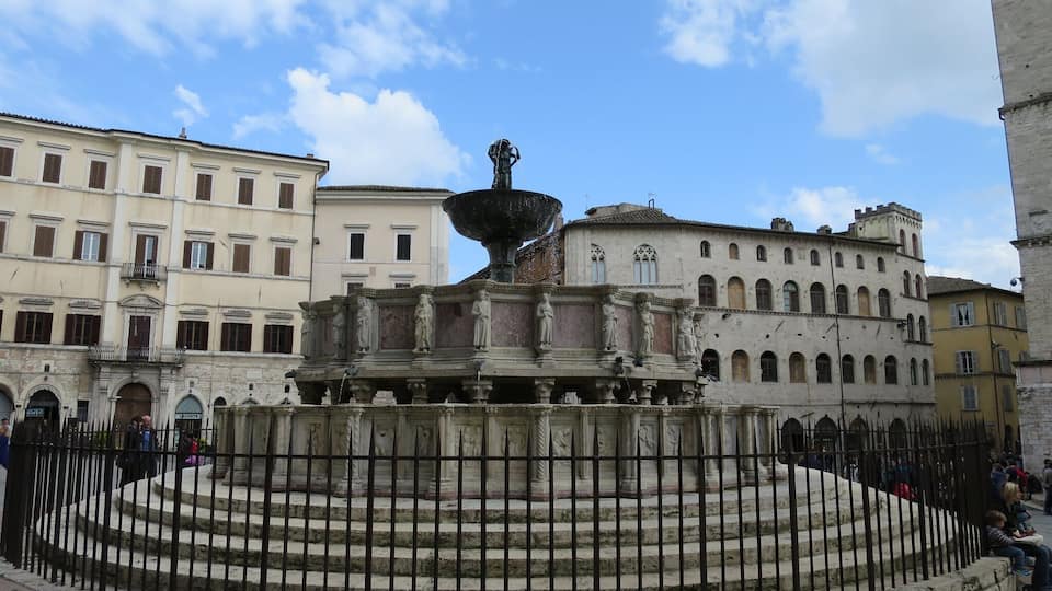 A historic fountain with statues in a square surrounded by classical architecture.