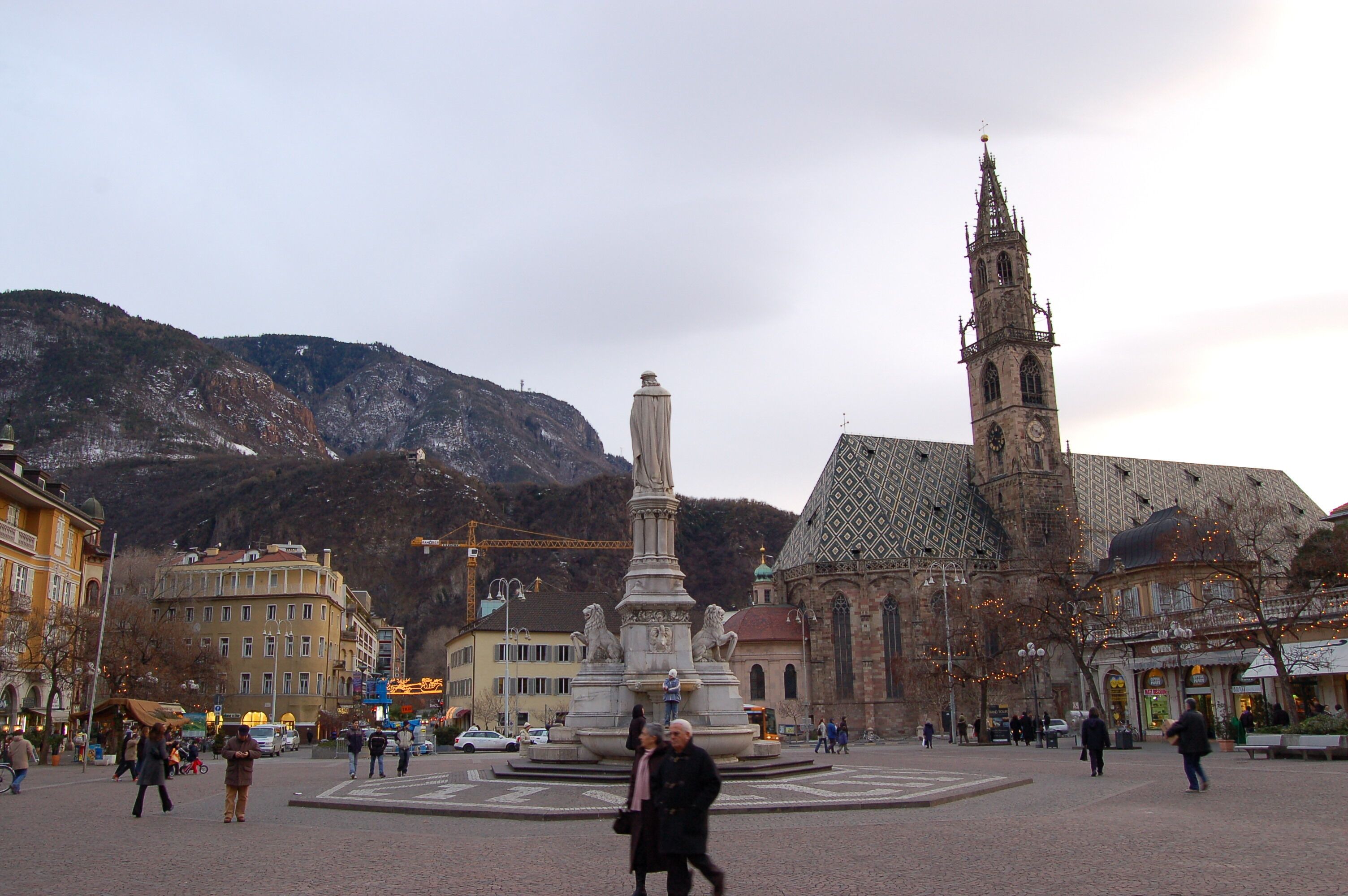 A square with a monument, a church, and mountains in the background.