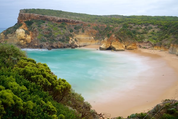 Eine Küstenlandschaft mit Sandstrand, türkisfarbenem Wasser und grünen Klippen.