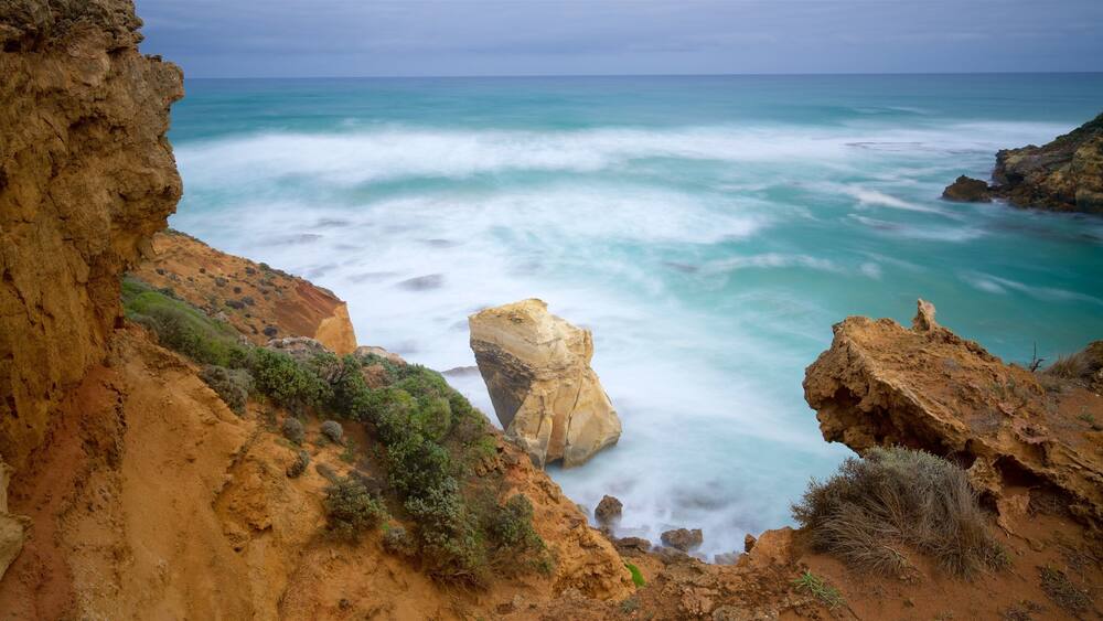 A coastal landscape with rocky cliffs, a prominent rock formation, and turquoise ocean waves.