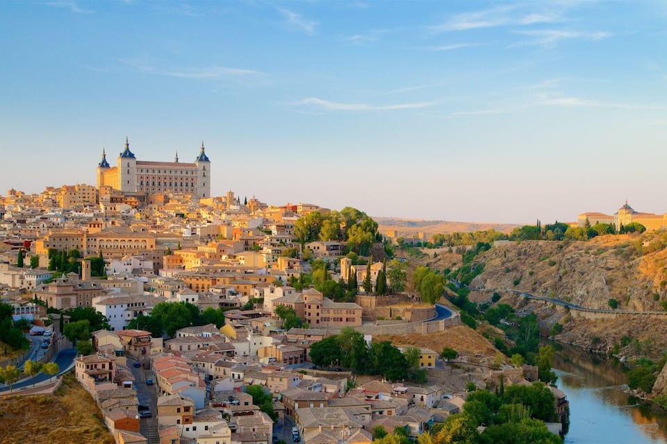 A historic cityscape with a prominent castle, a river, and surrounding hills.