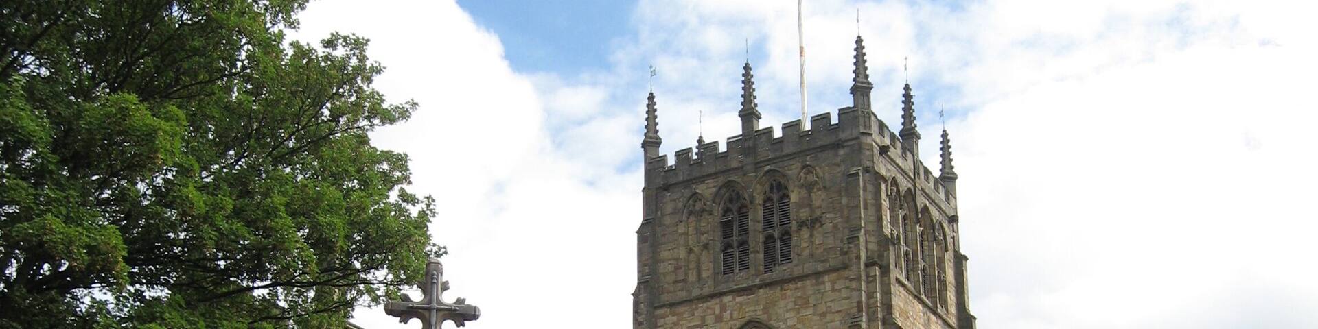 A historic church with a tall clock tower, surrounded by trees and a welcoming sign.
