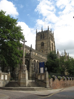 A historic church with a tall clock tower, surrounded by trees and a welcoming sign.
