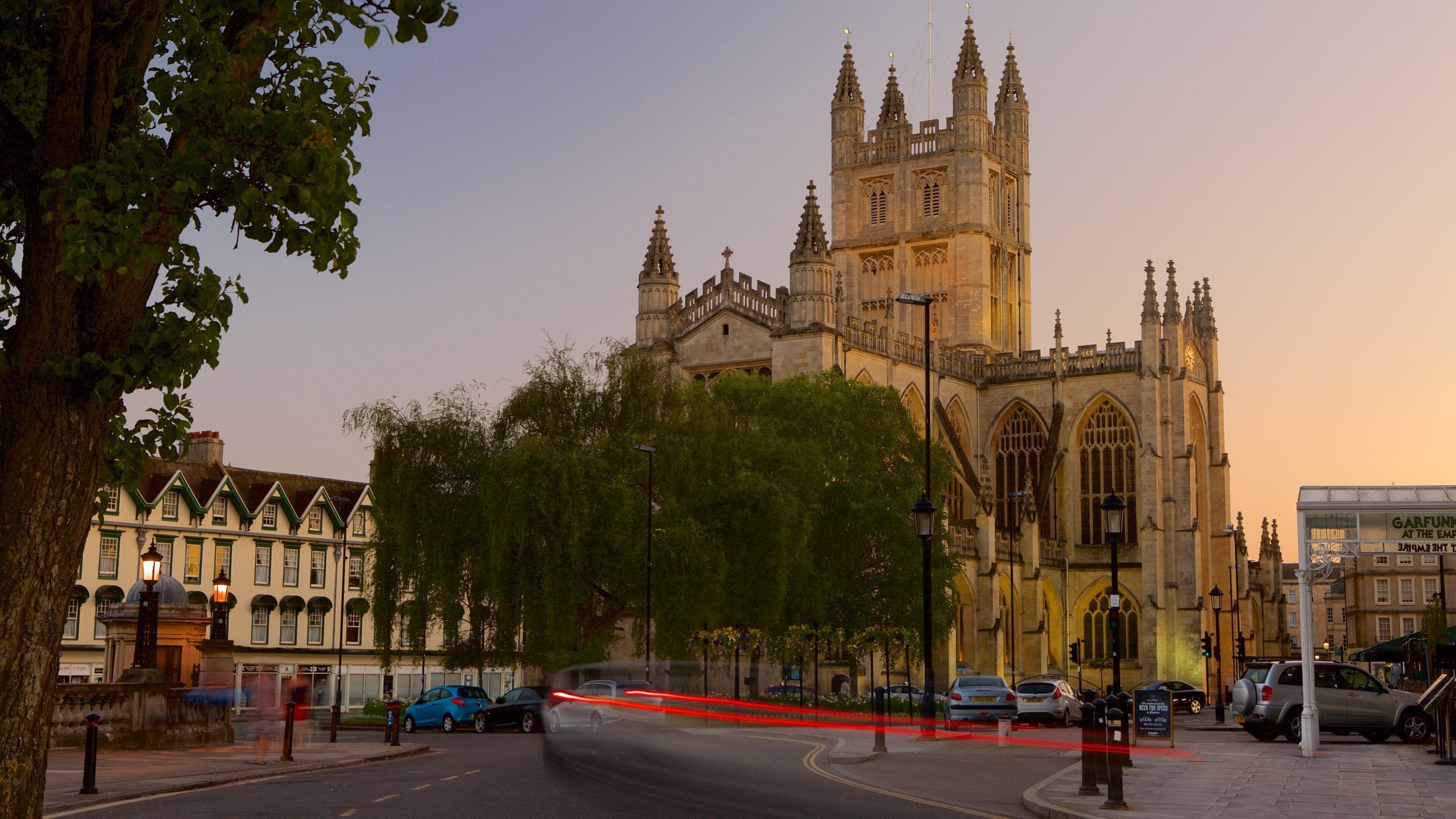 A historic cathedral with intricate architecture, a tree-lined street, and parked cars.