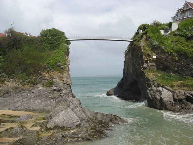Eine Küstenlandschaft mit einer Brücke über einem Felsen, Meereswellen und einem Haus auf dem Felsen.