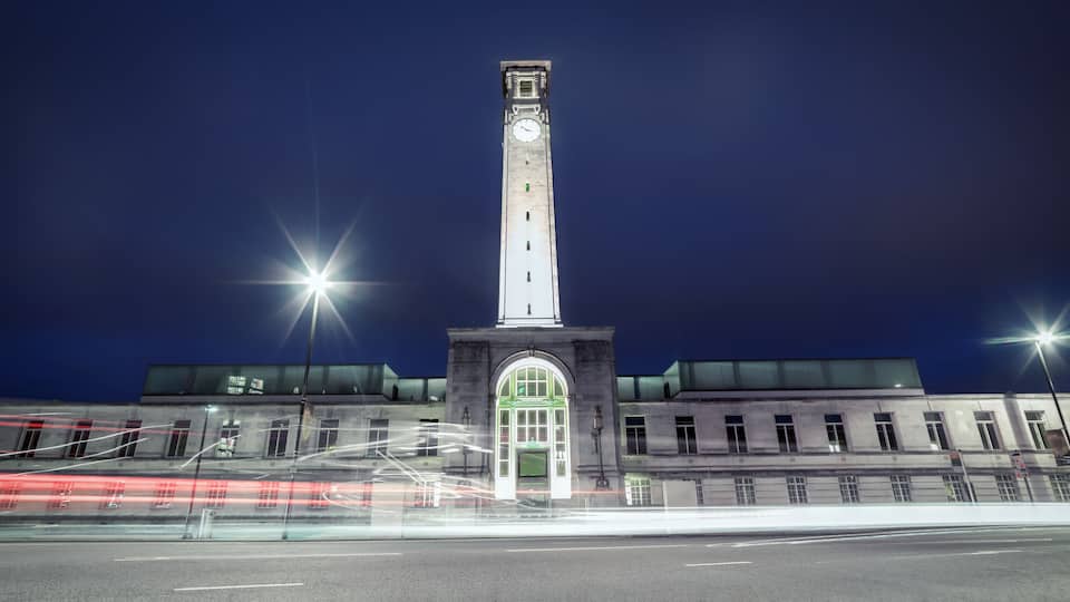 Una alta torre del reloj de noche, con farolas y estelas de luz dejadas por vehículos en movimiento.