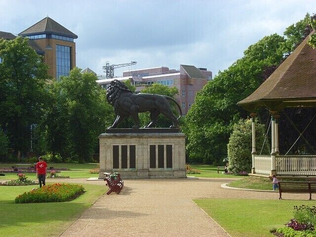 A park with a lion statue, a gazebo, and a building with a crane in the background.