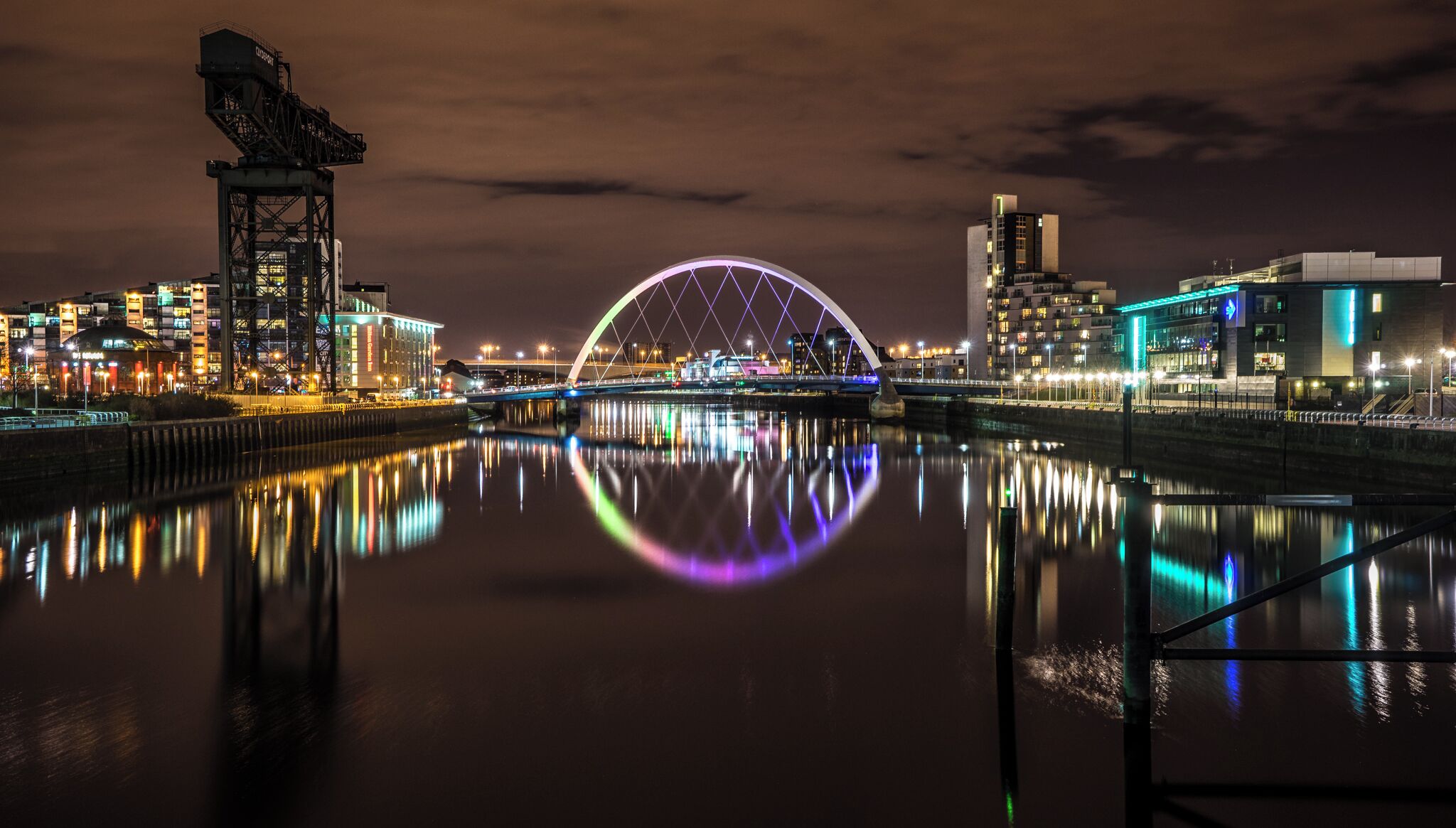 Un paisaje urbano nocturno con un puente iluminado que se refleja en el agua.