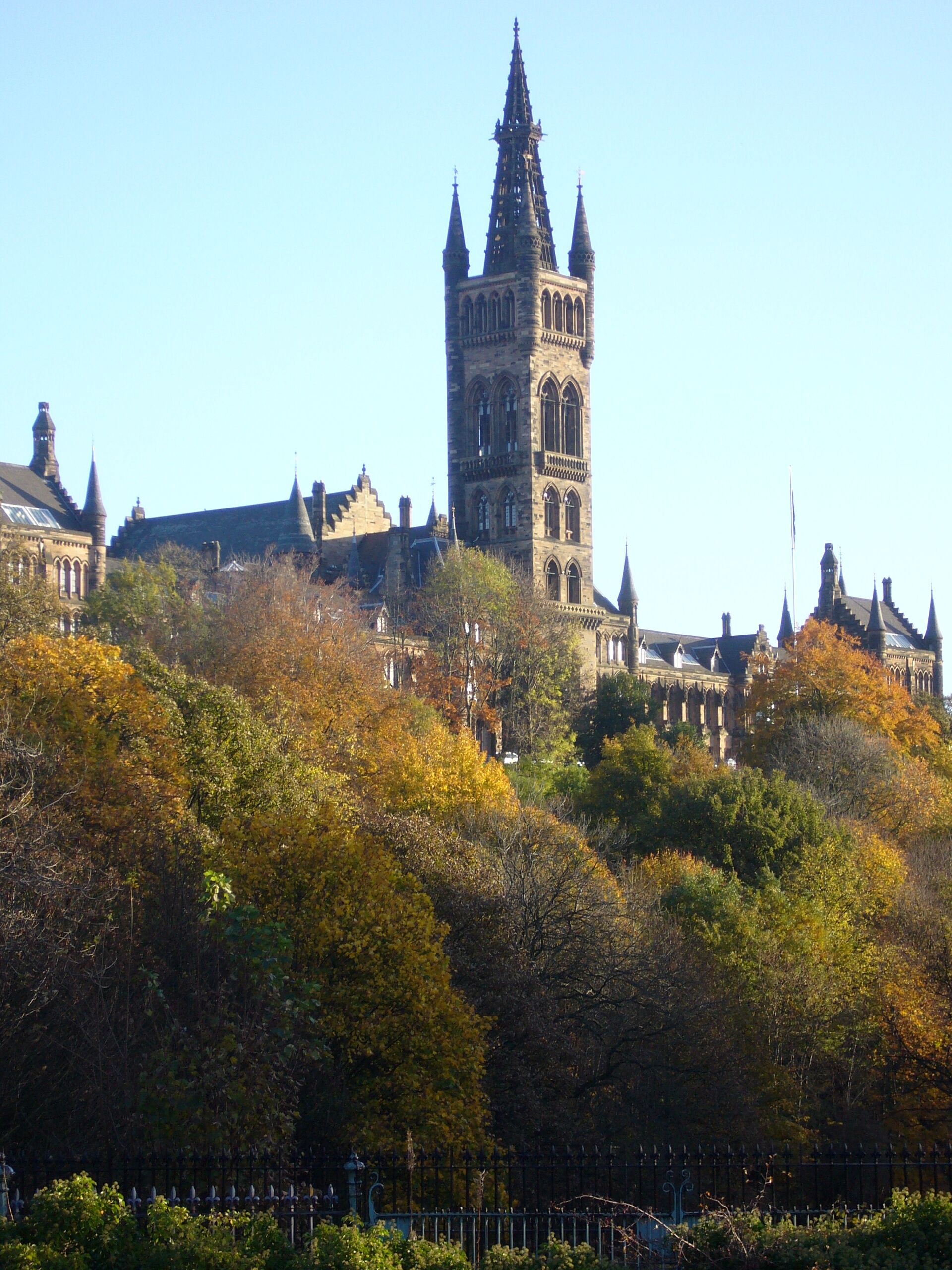 A historic building with a tall tower and spires, surrounded by autumn-colored trees.