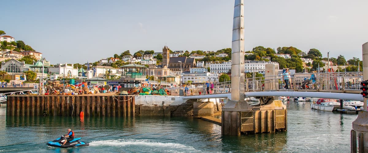 A waterfront with a jet ski, a tall tower, and a bustling harbor with boats and people.