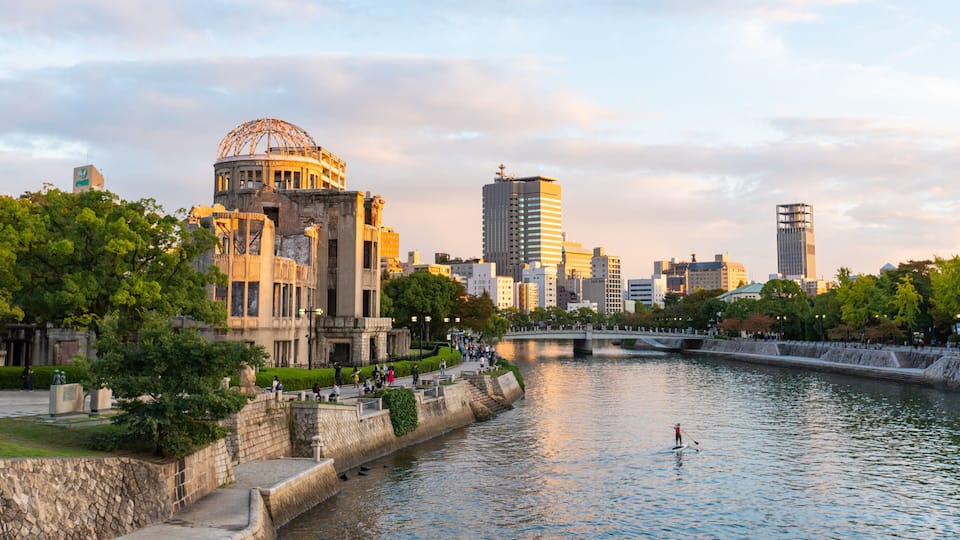A river with a bridge, a historic building with a dome, and modern skyscrapers in the background.