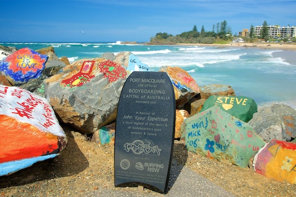 A beach with colorful rocks and a sign reading "Port Macquarie, the official Bodyboarding Capital of Australia."