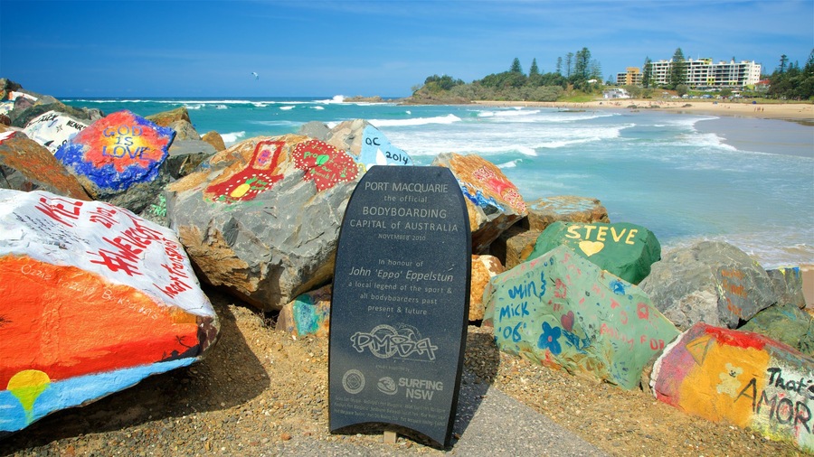 En strand med farverige sten og et skilt, der viser "Port Macquarie, Australiens officielle Bodyboarding-hovedstad".