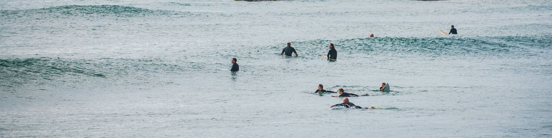 A coastal scene with surfers in the water, rocky cliffs, and a clear sky.
