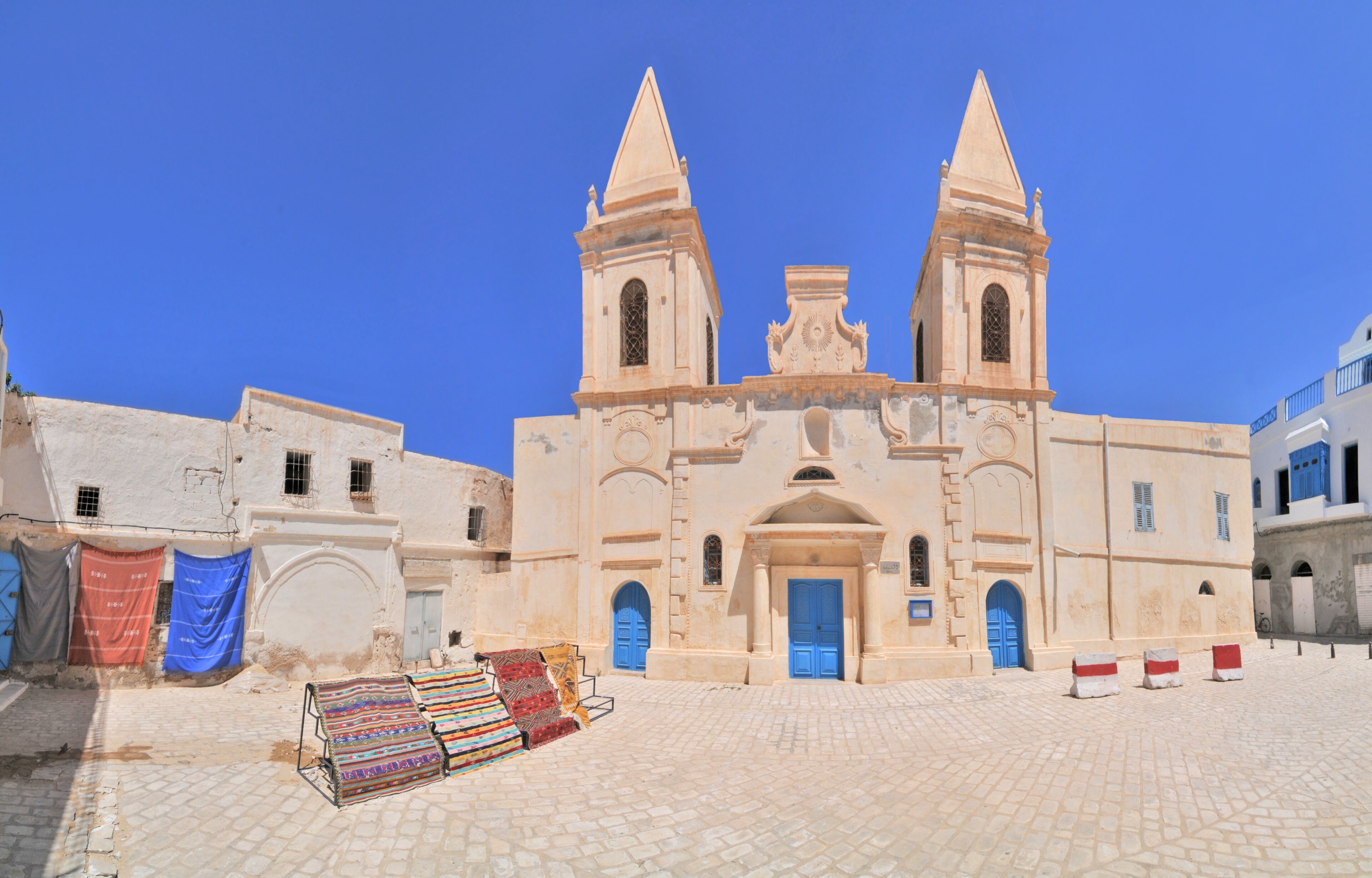 A historic church with two towers, a cobblestone square, and colorful textiles displayed outside.
