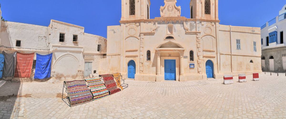 A historic church with two towers, a cobblestone square, and colorful textiles displayed outside.