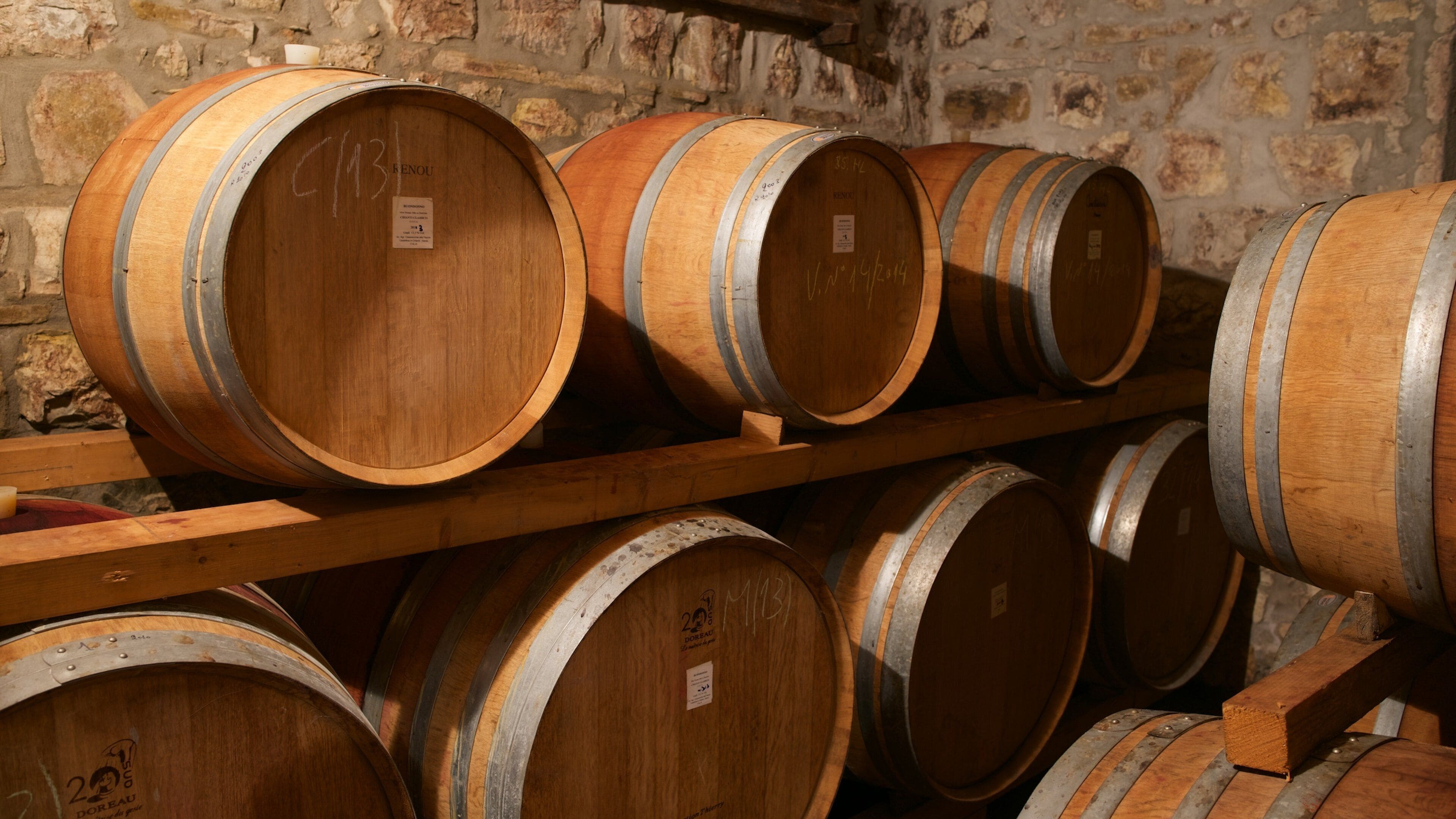 Wooden wine barrels stacked on shelves in a cellar with stone walls.