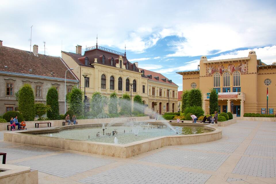 A public square with a fountain, benches, and historic buildings.