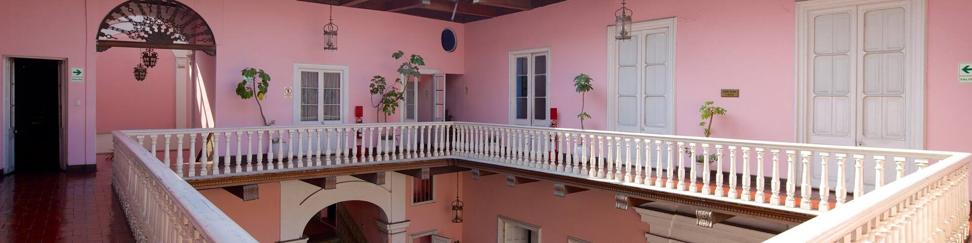 A pink building with a white balcony railing, a staircase, and a wooden floor.