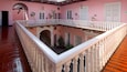 A pink building with a white balcony railing, a staircase, and a wooden floor.