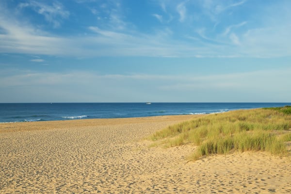 A sandy beach with gentle waves and a boat in the distance.