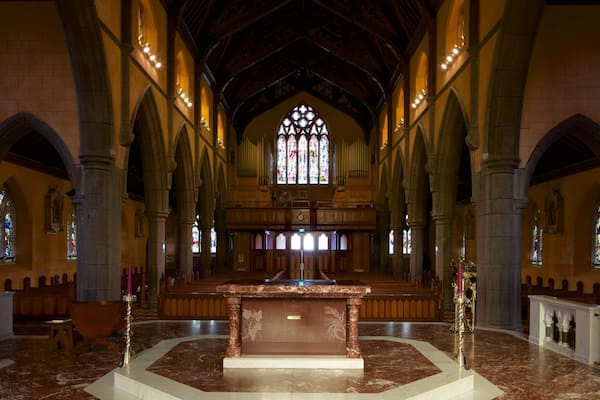 Interior de igreja com piso de mármore, bancos de madeira e janelas de vitrais.
