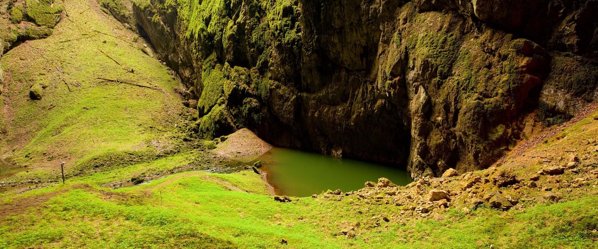 A green valley with a small pond surrounded by rocky cliffs.