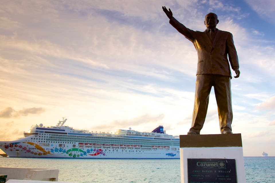 Une statue représentant un homme les bras levés, un navire de croisière en arrière-plan et un ciel dégagé.