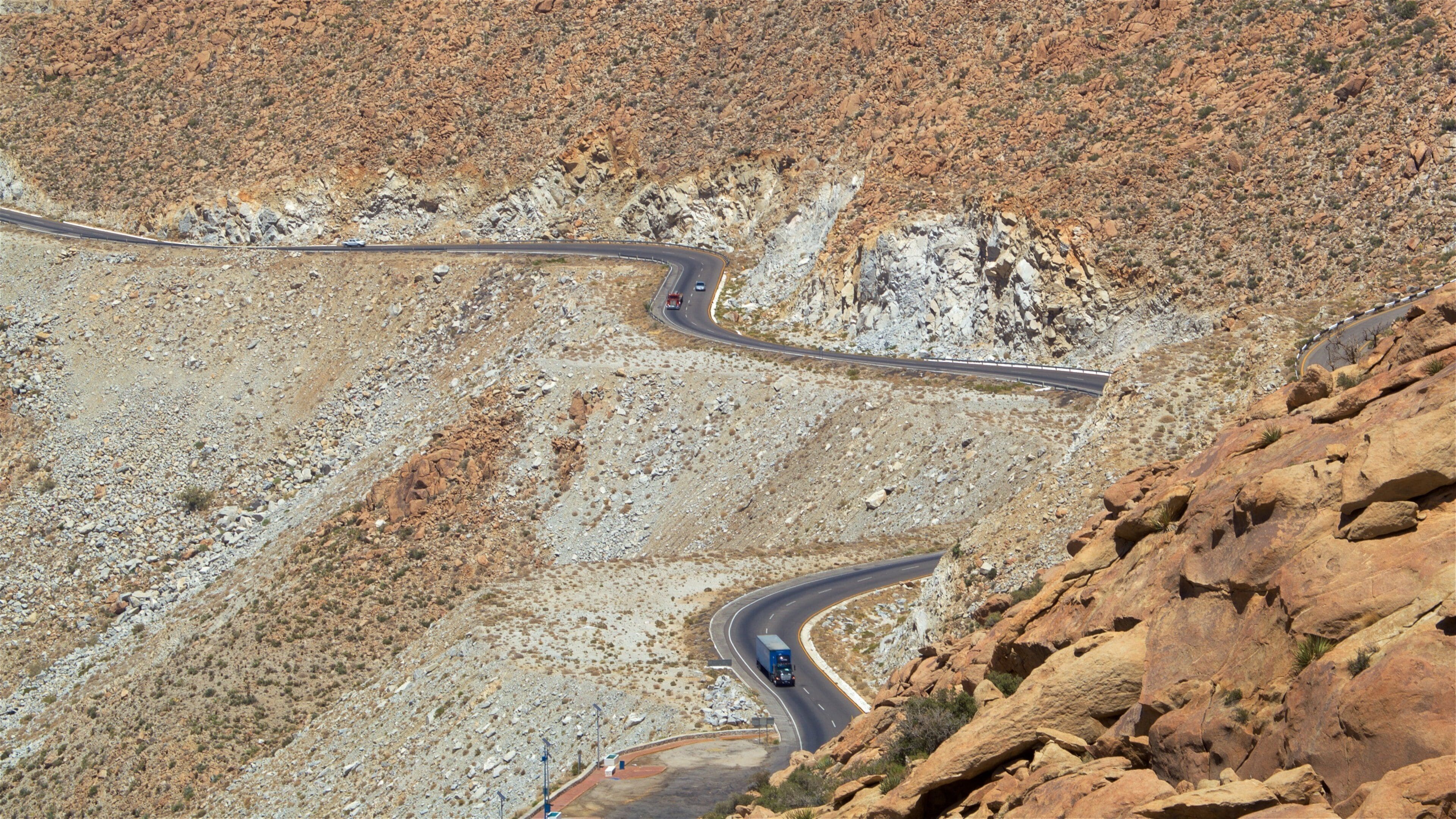 A winding mountain road with rocky terrain and sparse vegetation.
