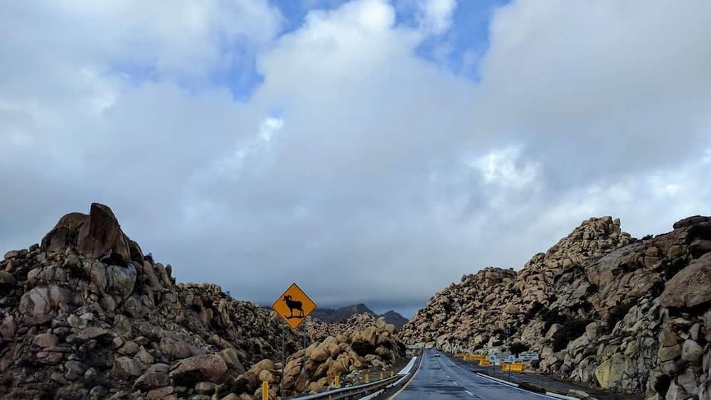 A road flanked by large rocks under a cloudy sky.