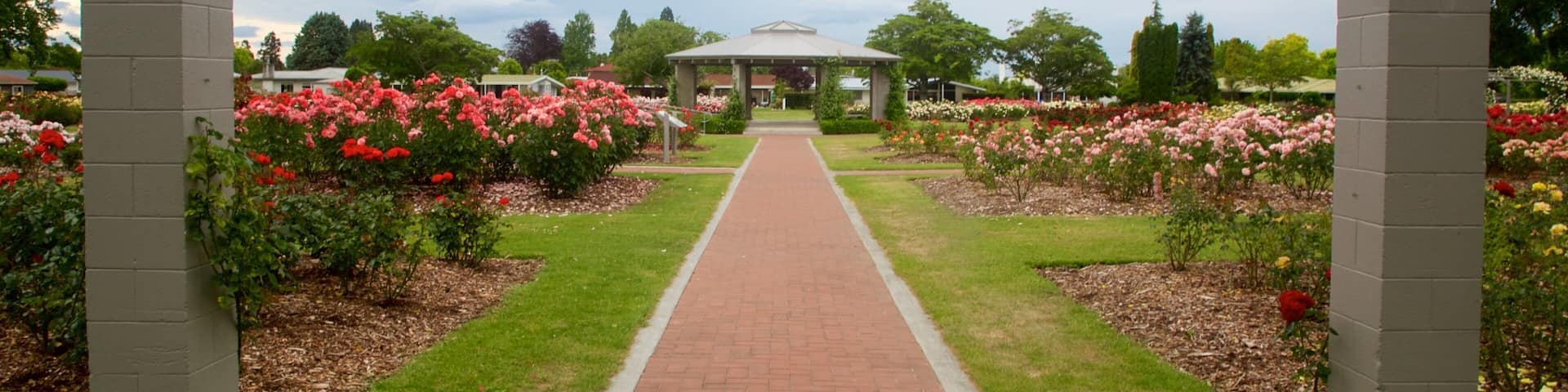 A garden pathway leading to a gazebo surrounded by flower beds.