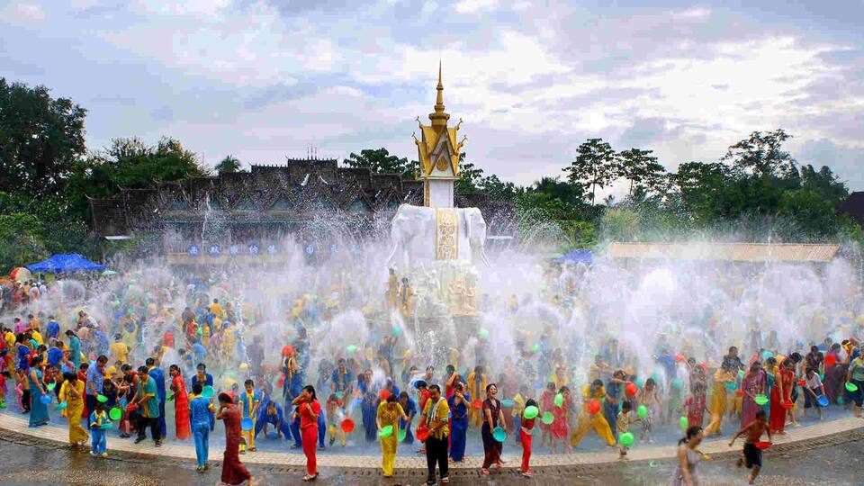 A water fountain with a golden spire in the center, surrounded by a crowd of people.