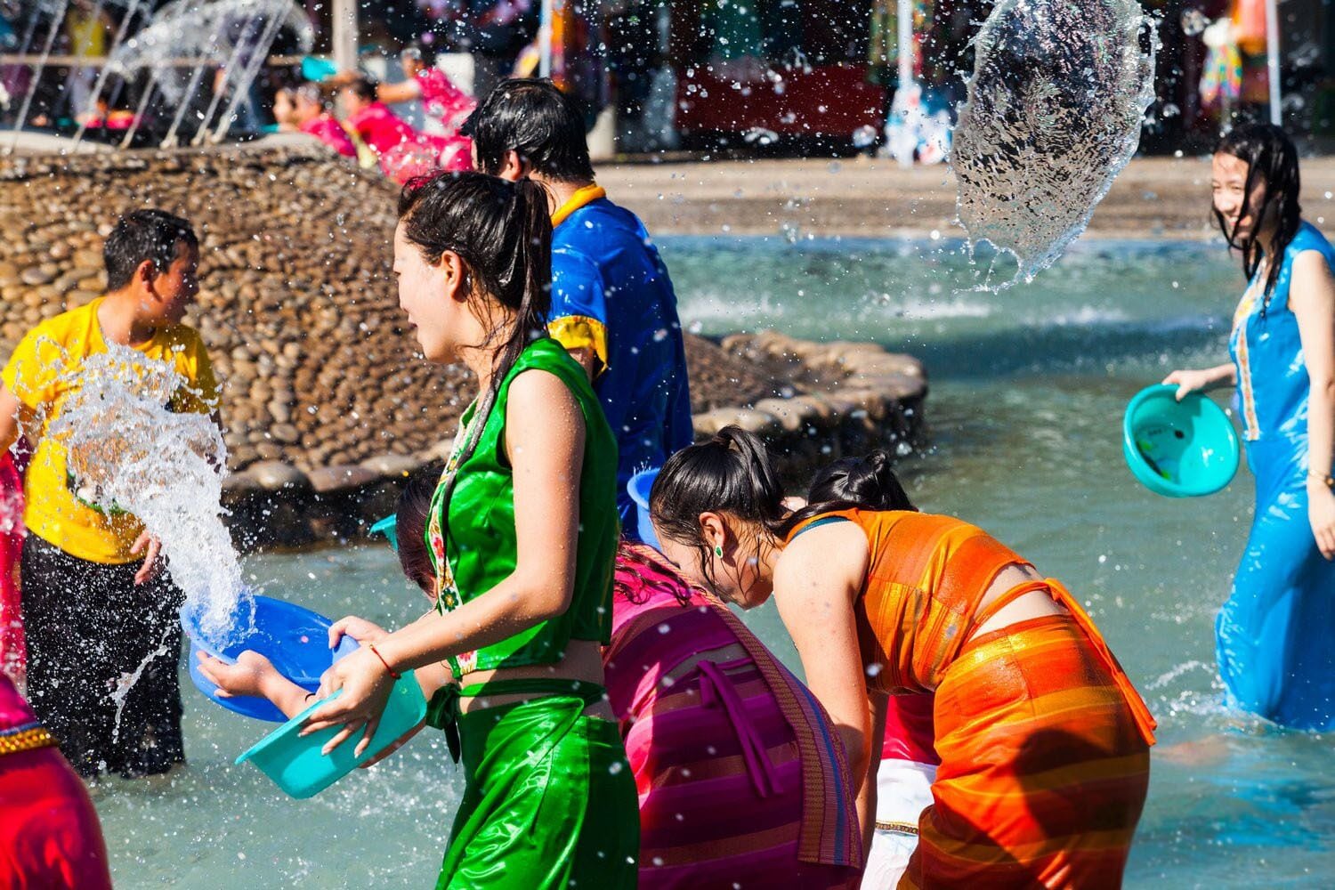 A group of people playing in a water fountain with water splashing around them.