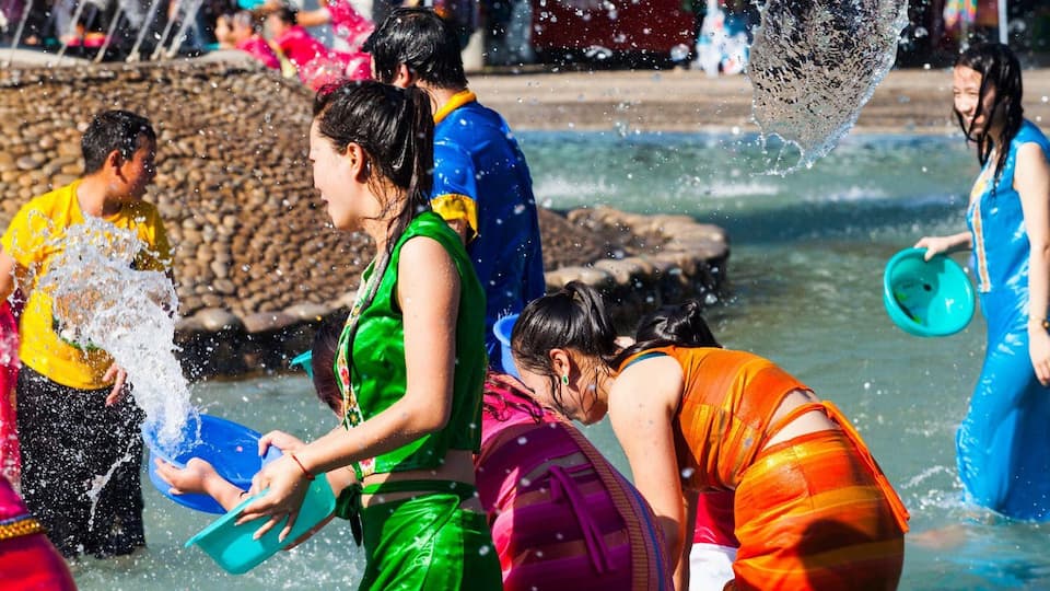 A group of people playing in a water fountain with water splashing around them.