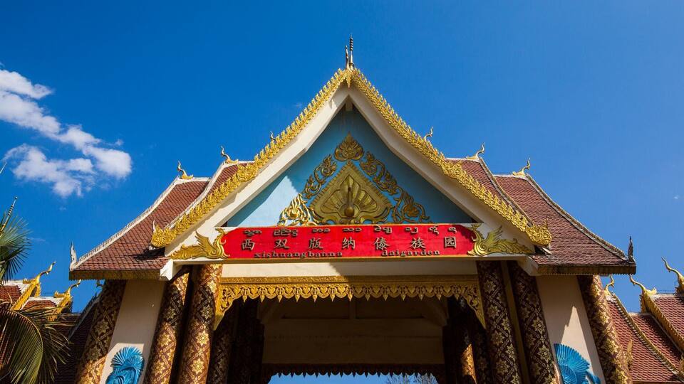 A traditional Thai temple with ornate golden decorations and a red banner with white text.