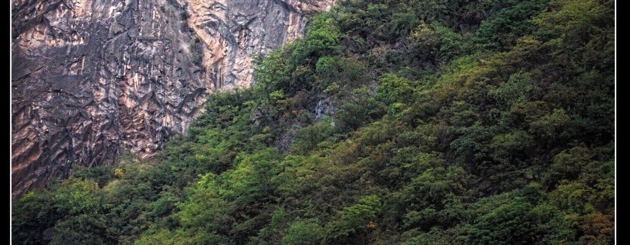 Una pagoda roja sobre una colina verde y exuberante, con un acantilado escarpado al fondo.