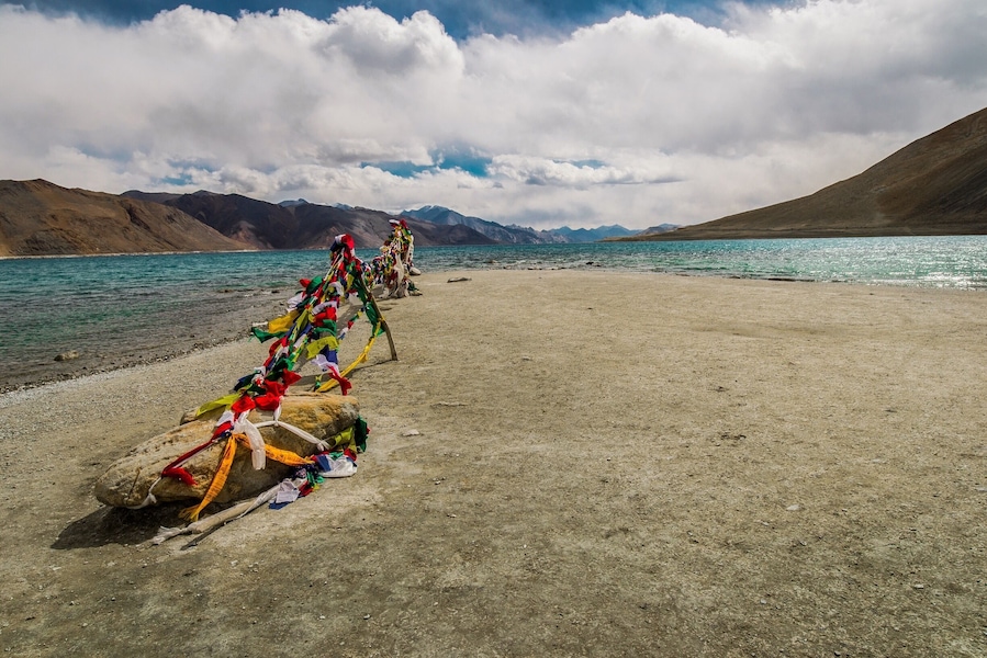 Un lac paisible, bordé de drapeaux de prières aux couleurs vives, avec des montagnes en toile de fond.
