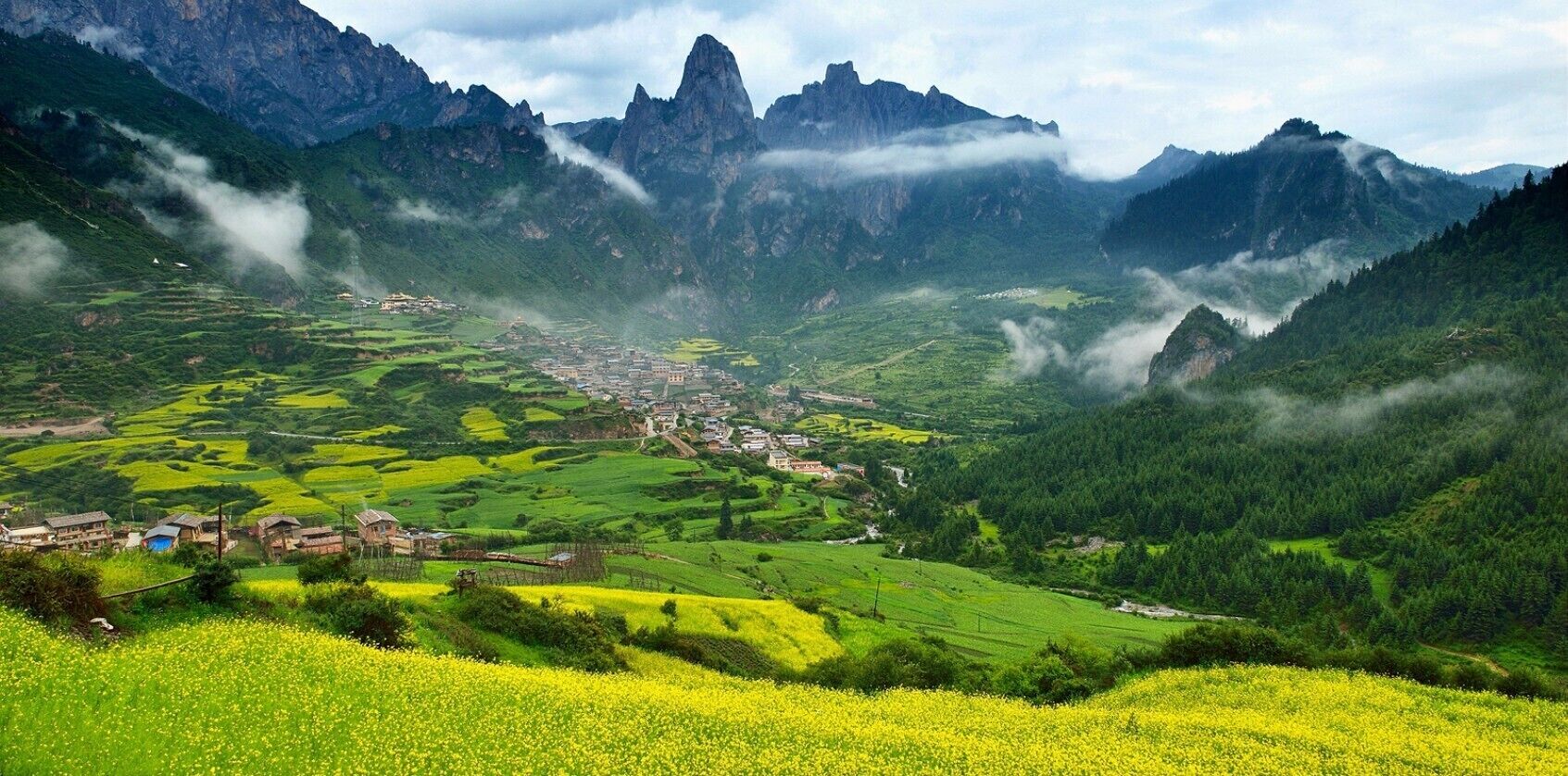 A valley with terraced fields, a small village, and towering mountains.