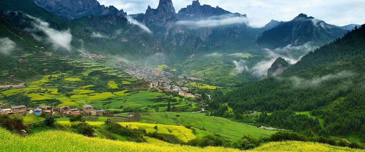 A valley with terraced fields, a small village, and towering mountains.