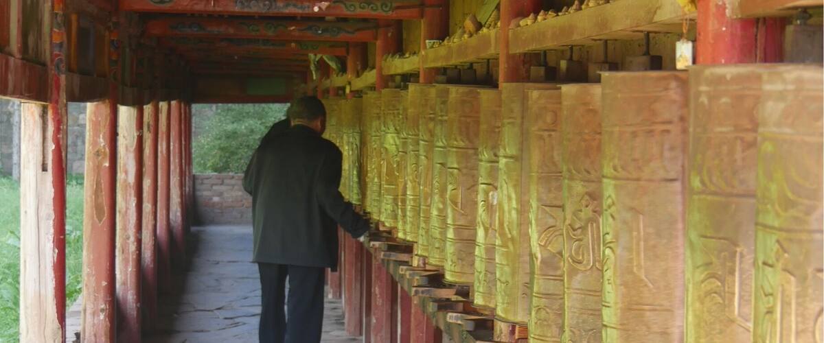 A person walking along a corridor with ornate pillars and prayer wheels.