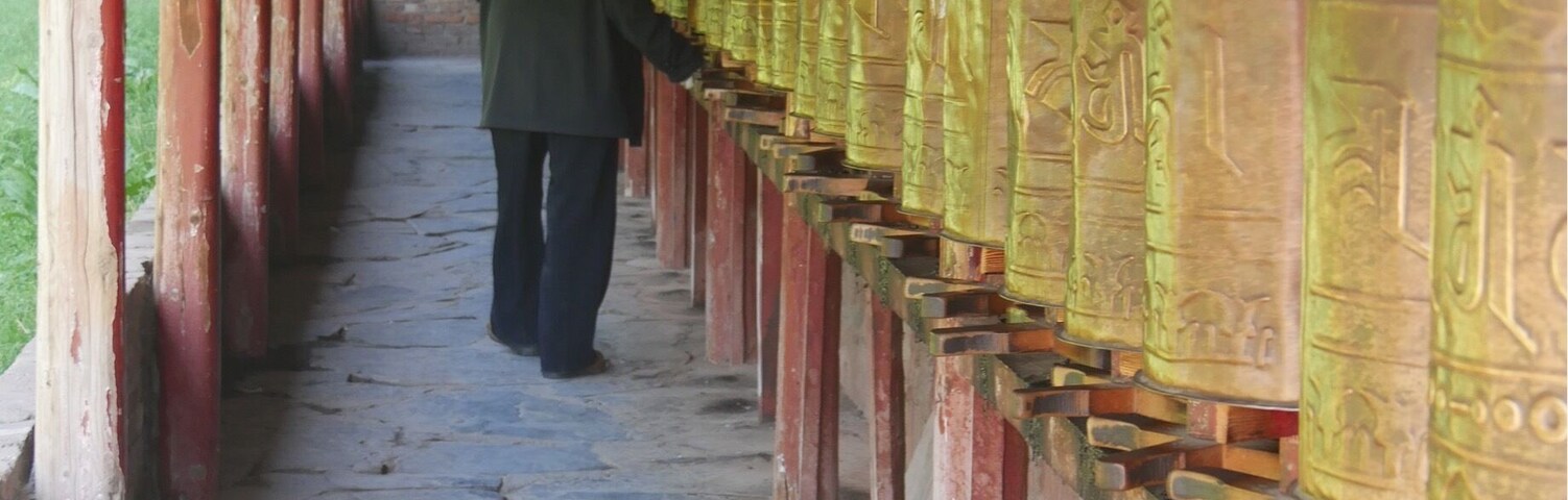 A person walking along a corridor with ornate pillars and prayer wheels.