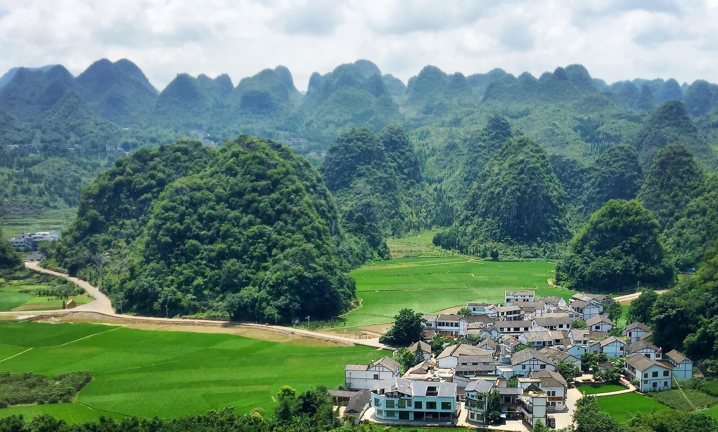 A village nestled in a valley surrounded by lush green hills and mountains.