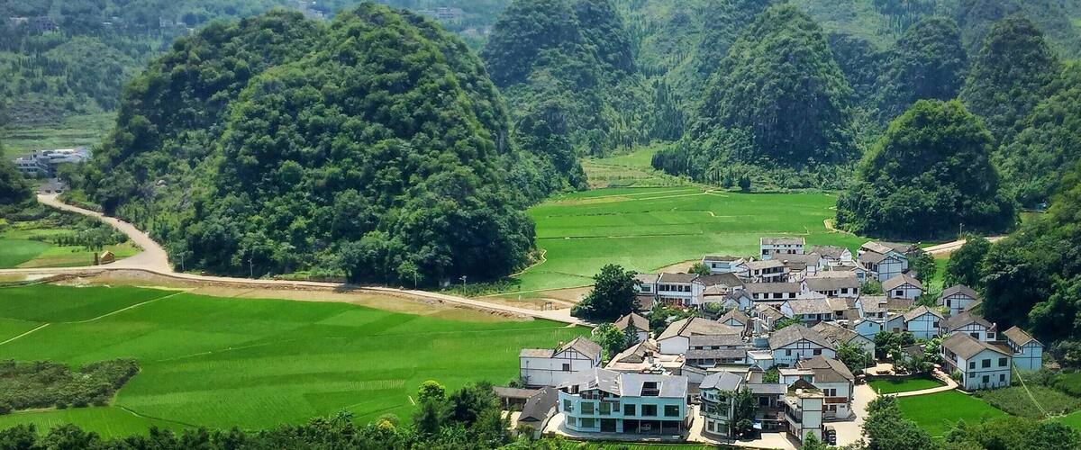 A village nestled in a valley surrounded by lush green hills and mountains.