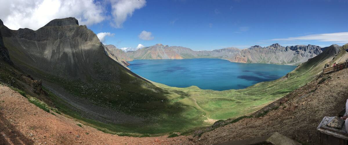 A panoramic view of a deep blue lake surrounded by rugged mountains and green hills.