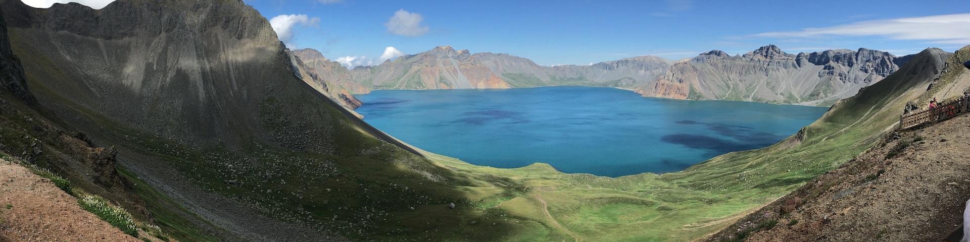 A panoramic view of a deep blue lake surrounded by rugged mountains and green hills.