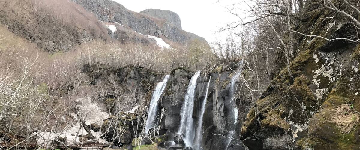 A waterfall cascading into a clear turquoise lake surrounded by rocky terrain and sparse vegetation.