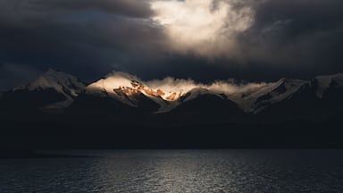 Una cordillera con picos nevados y una masa de agua al frente.