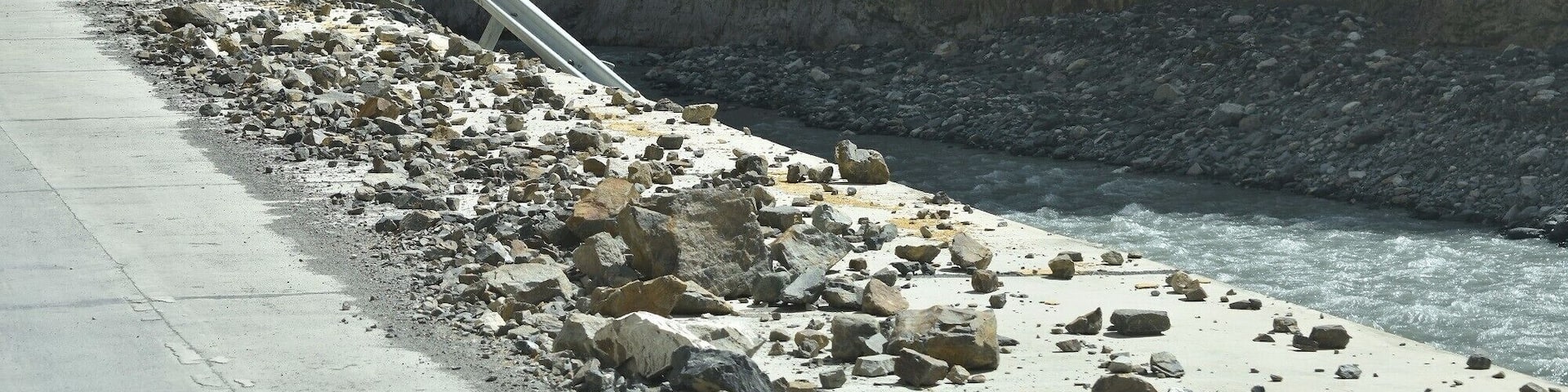 A coastal road with a guardrail, rocky terrain, and a cliff.